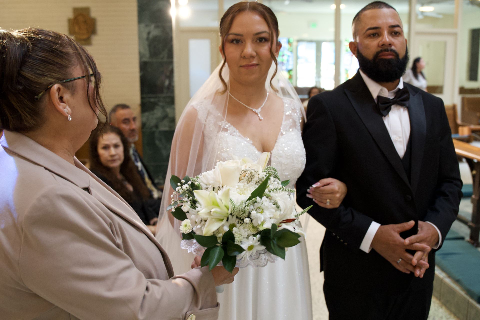 Bride walking down church aisle with bouquet, escorted by a man in a black suit