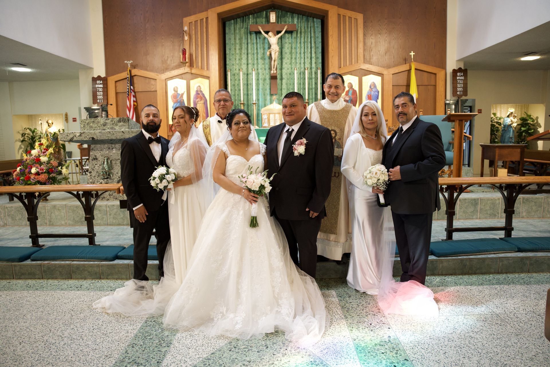 Wedding party posing at the altar, with bride in white gown and groom in black suit, flanked by attendants.