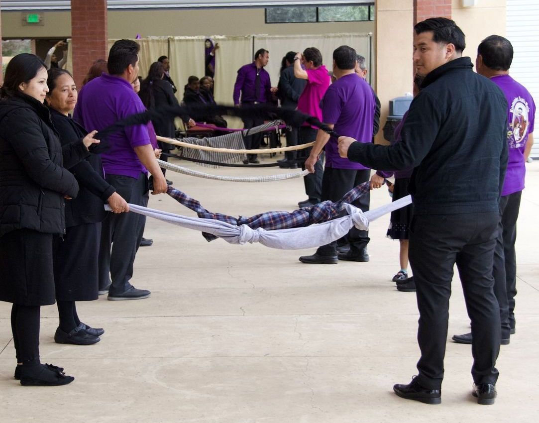 People in purple shirts and black pants hold ribbons in a mirrored outdoor performance line.