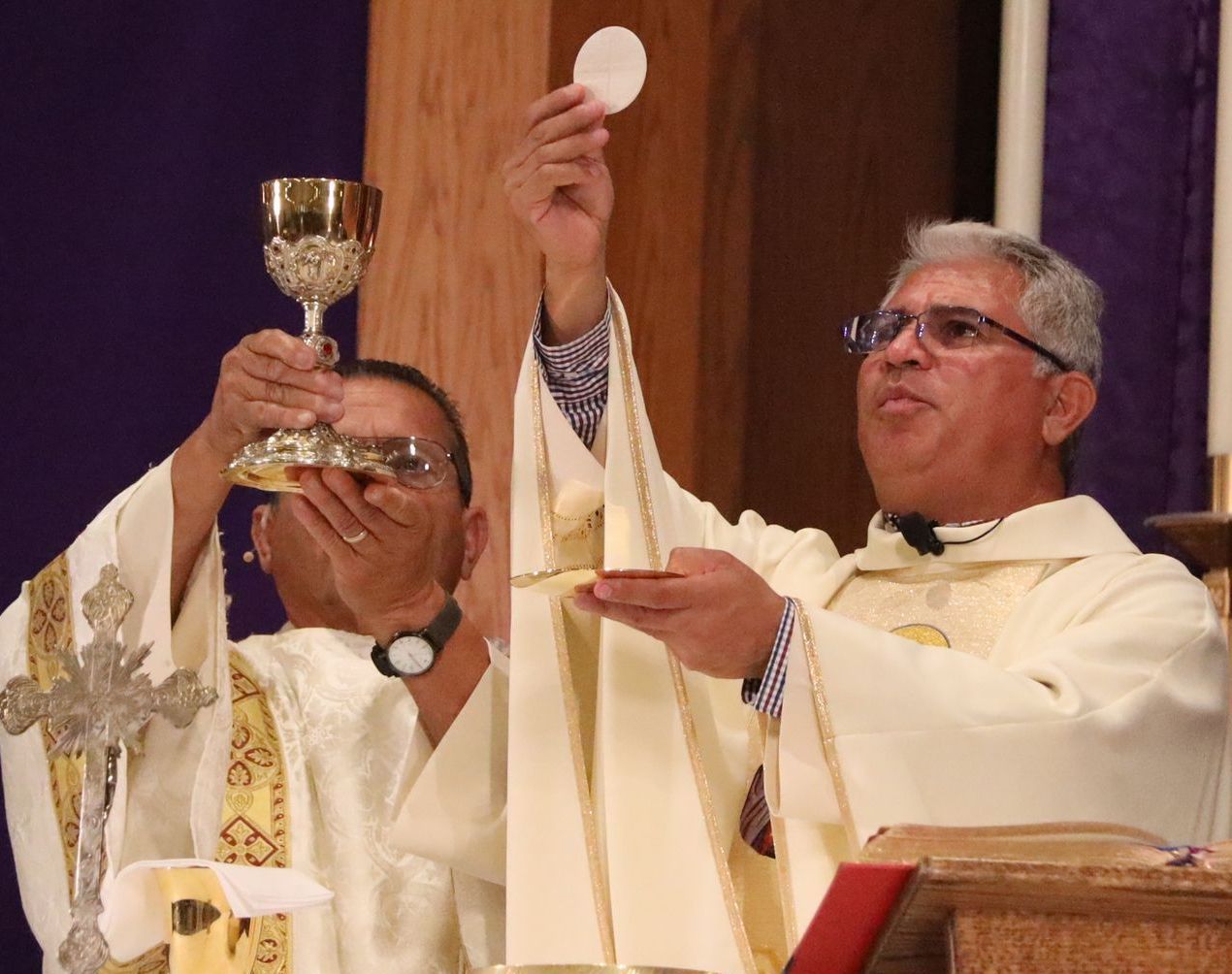 Priests at the altar during communion, one holding up a host and another a chalice.