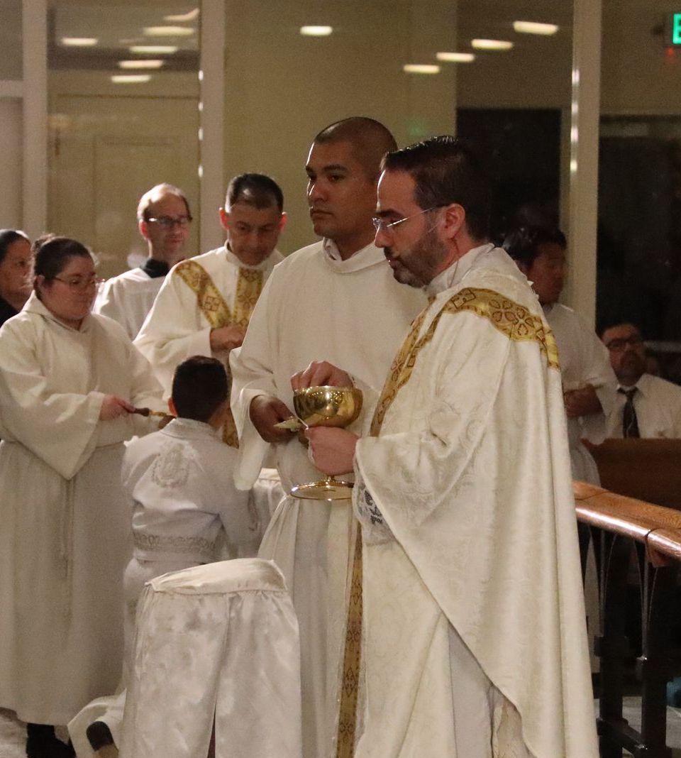 Clergy in white robes holding a golden chalice during a church ceremony