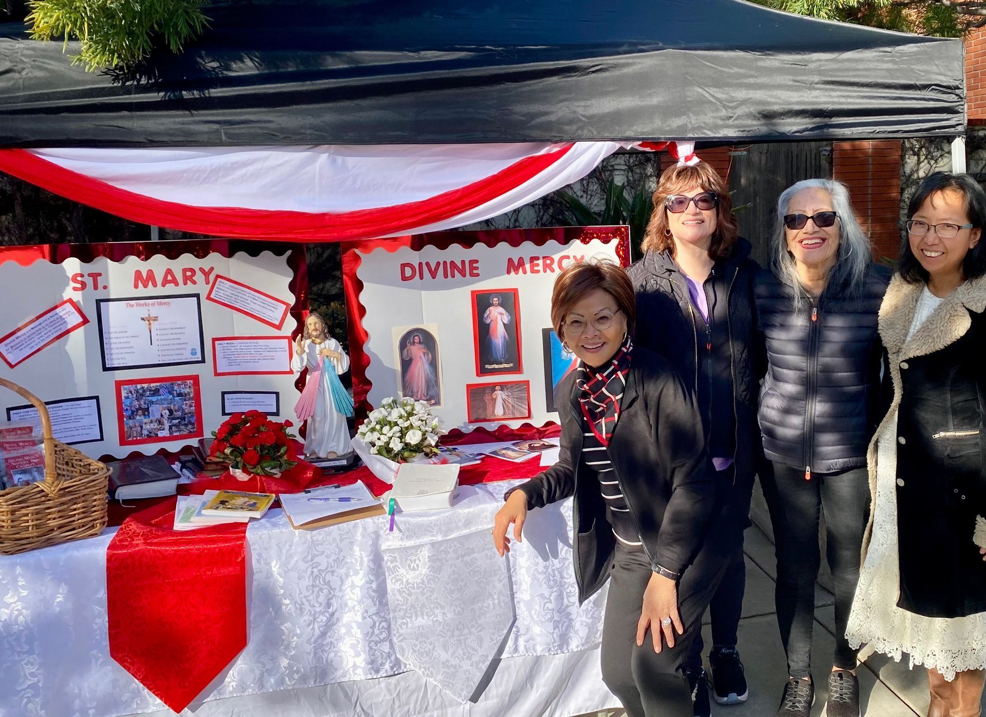 Outdoor church display booth with red-and-white decor and four people standing beside it