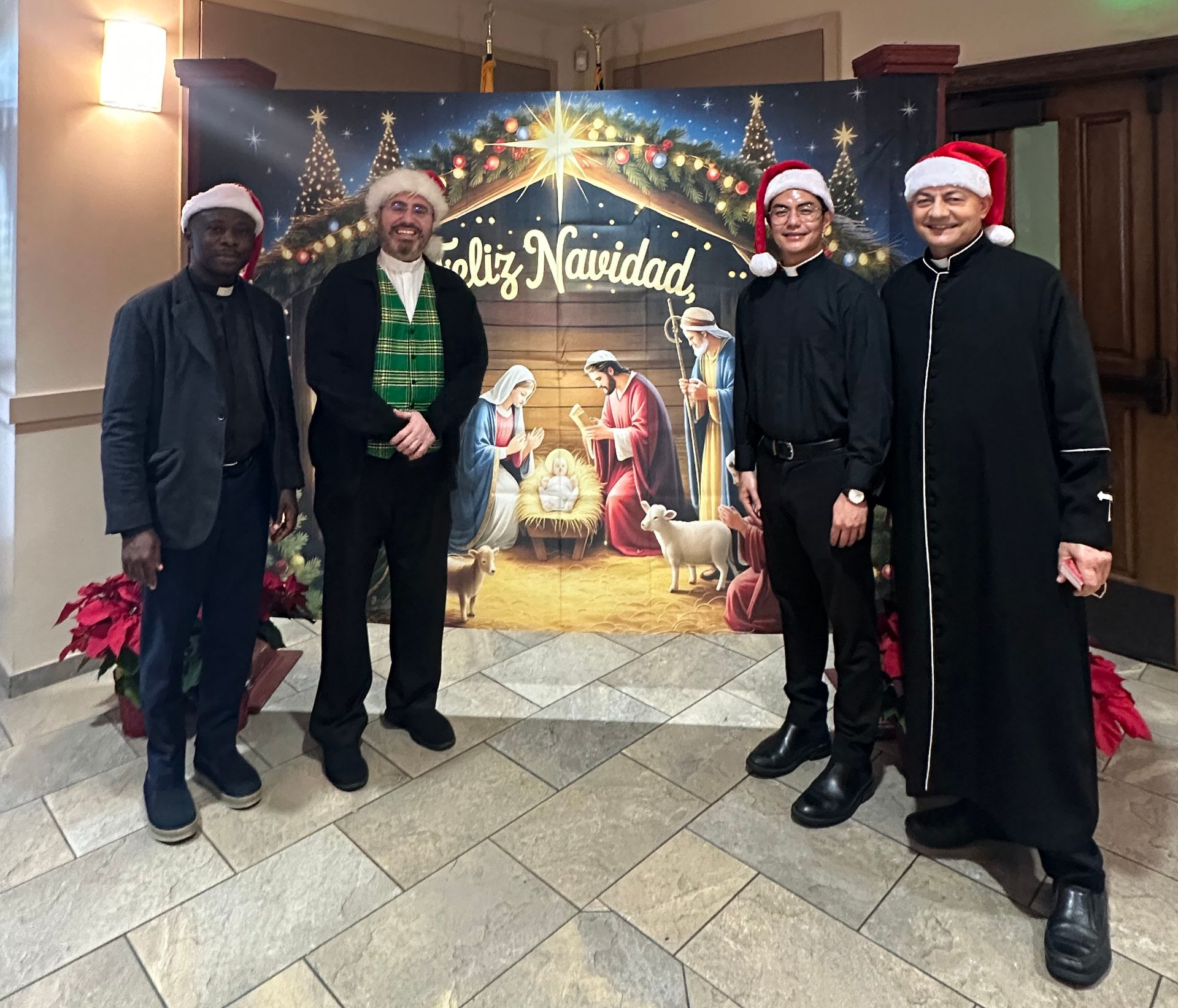 Four people in Santa hats pose at a holiday display reading “Feliz Navidad.”