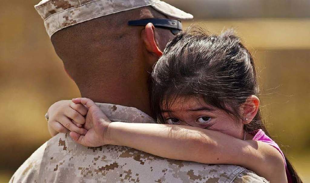 A child clings to a soldier’s shoulder, peering over with a somber expression.