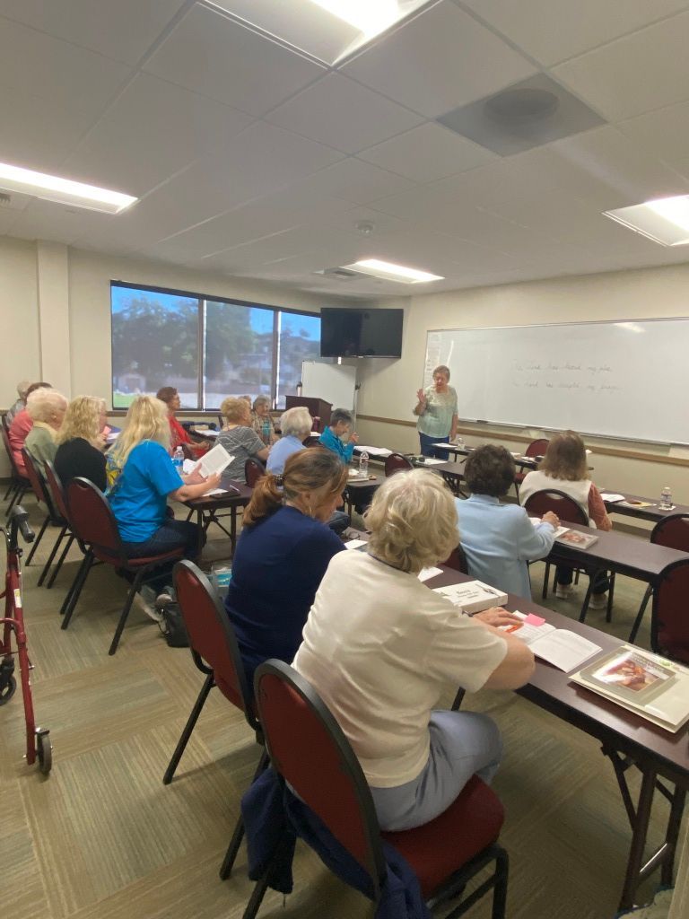 Audience seated in a classroom meeting, facing a presenter near the whiteboard