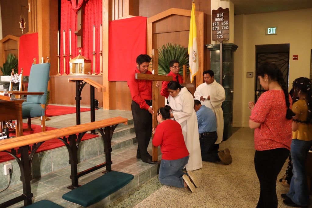 People gathered inside a church near the altar, with one person kneeling and others standing nearby.