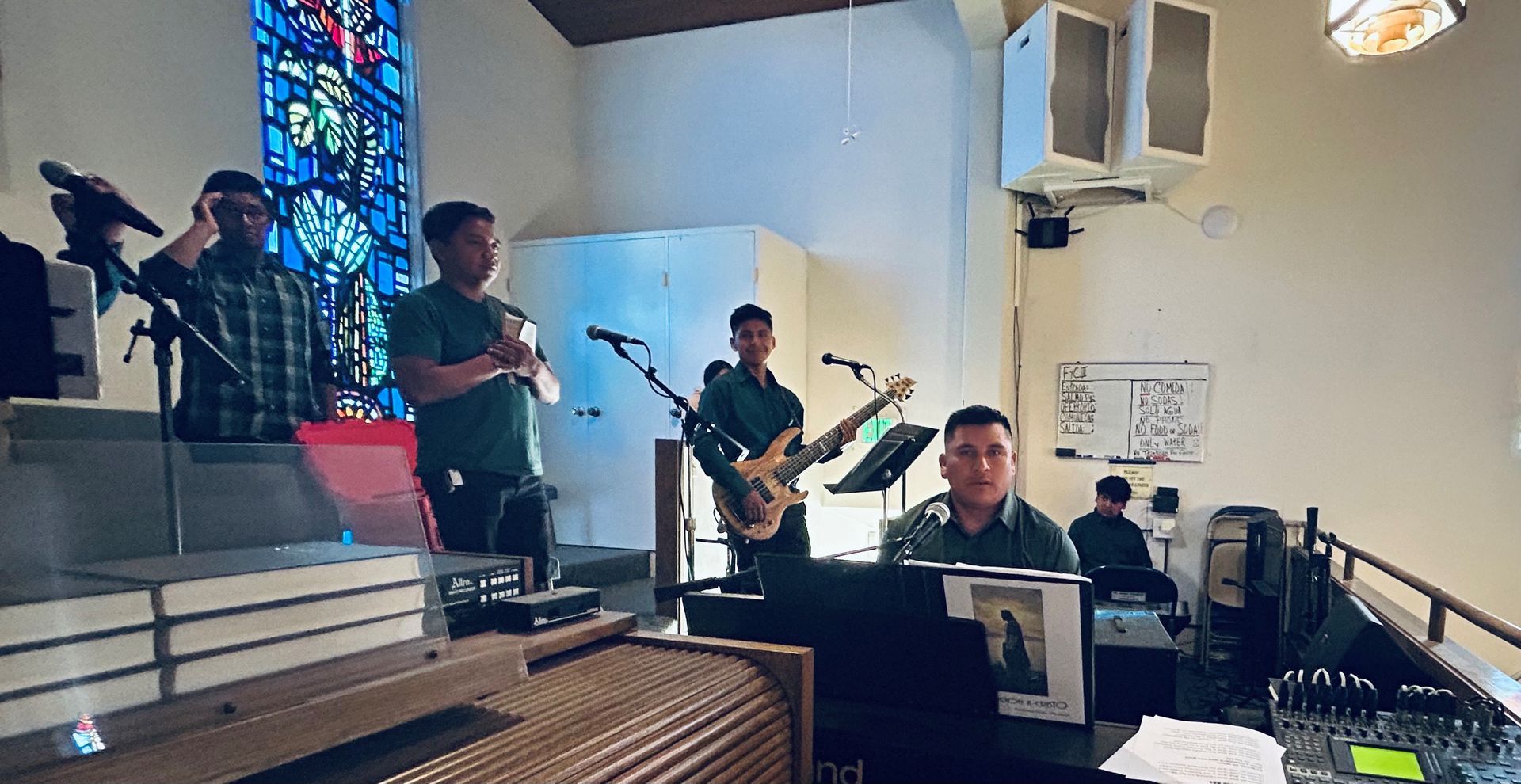 Band performing live in a small church, with musicians on stage and a sound booth in front