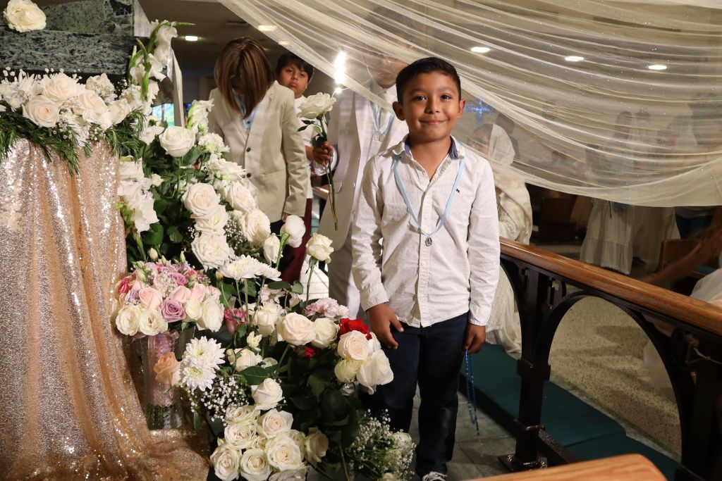 Child smiling on a decorated indoor walkway beside white and pink floral arrangements