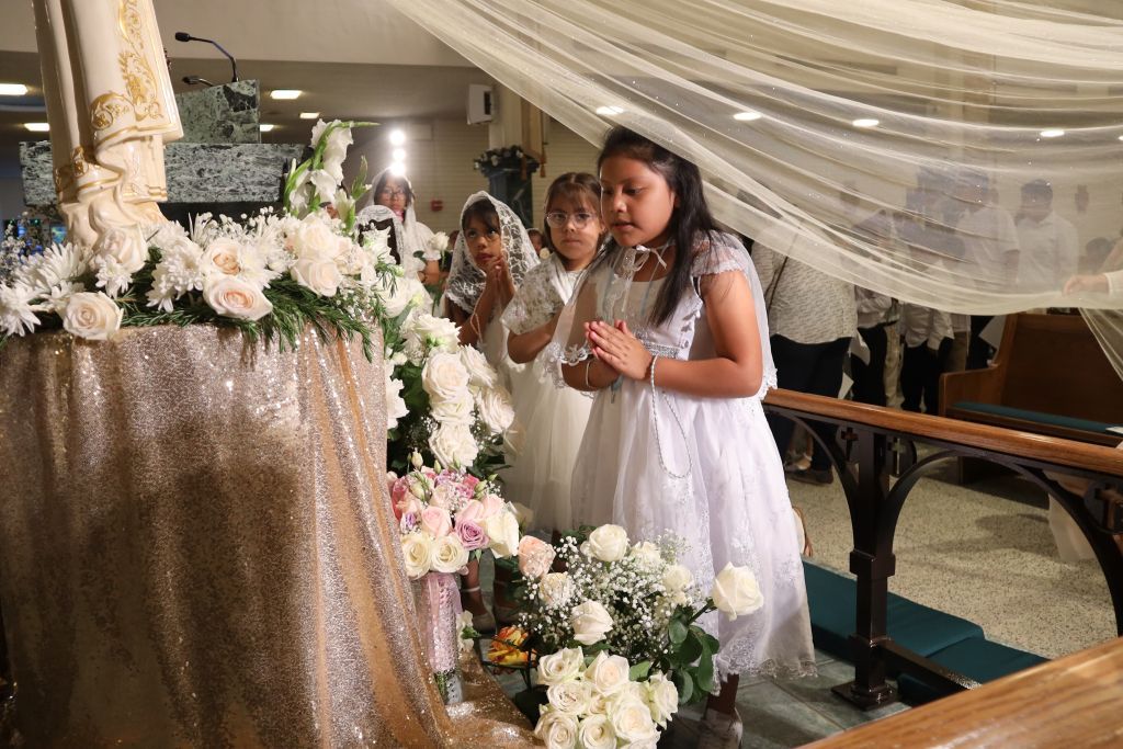 Two girls in white dresses standing on a decorated staircase at an event, surrounded by white flowers and draped fabric