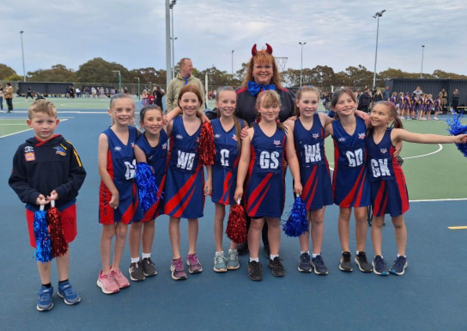 Youth cheer team posing on a blue field in red, white, and blue uniforms, smiling with arms raised.