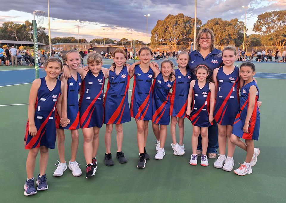 Youth sports team in blue and red uniforms posing on an outdoor court at sunset
