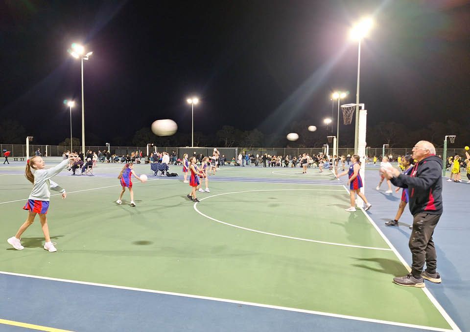People playing on a lit outdoor court at night, with spectators along the sideline.
