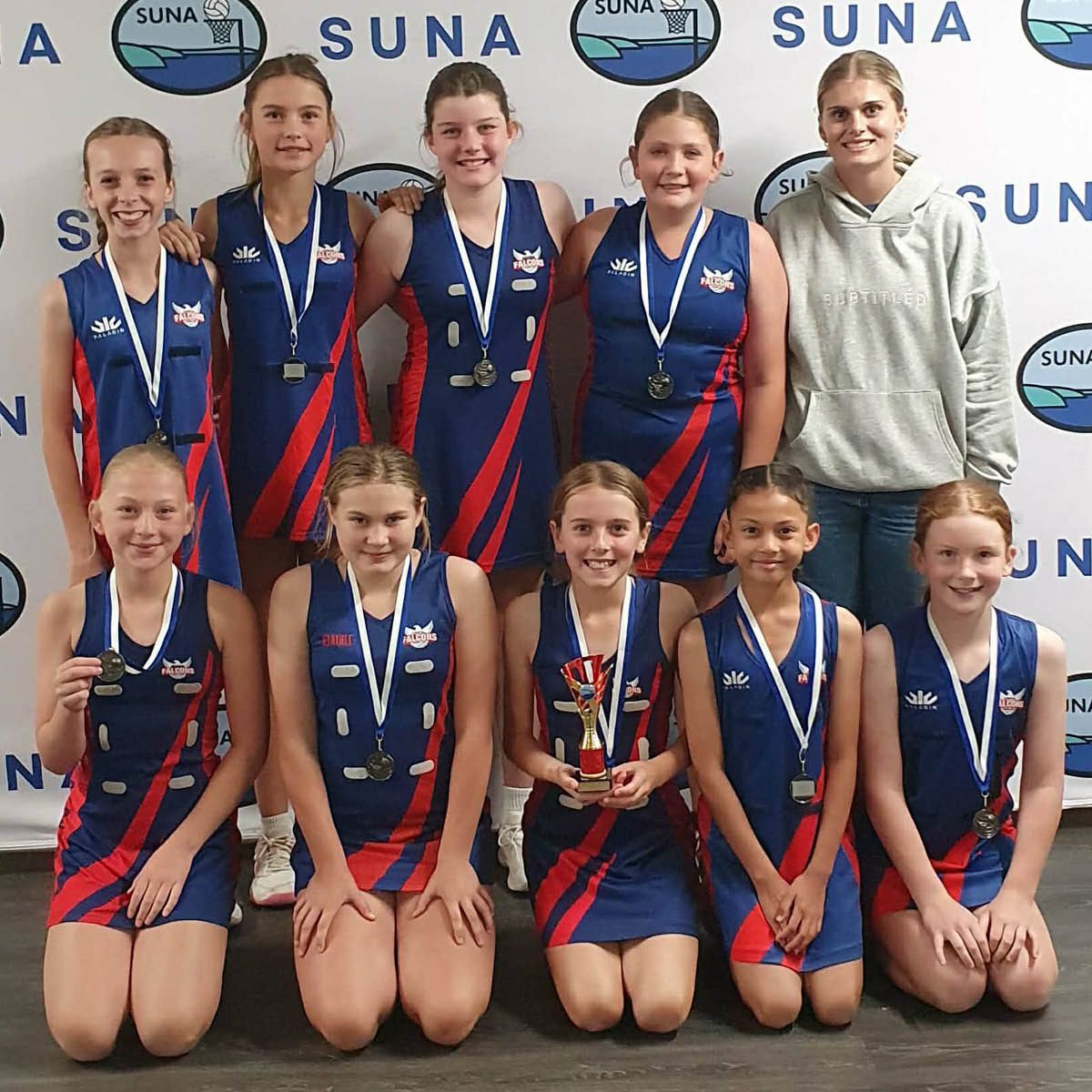 Youth netball team posing with medals in front of a SUNA backdrop