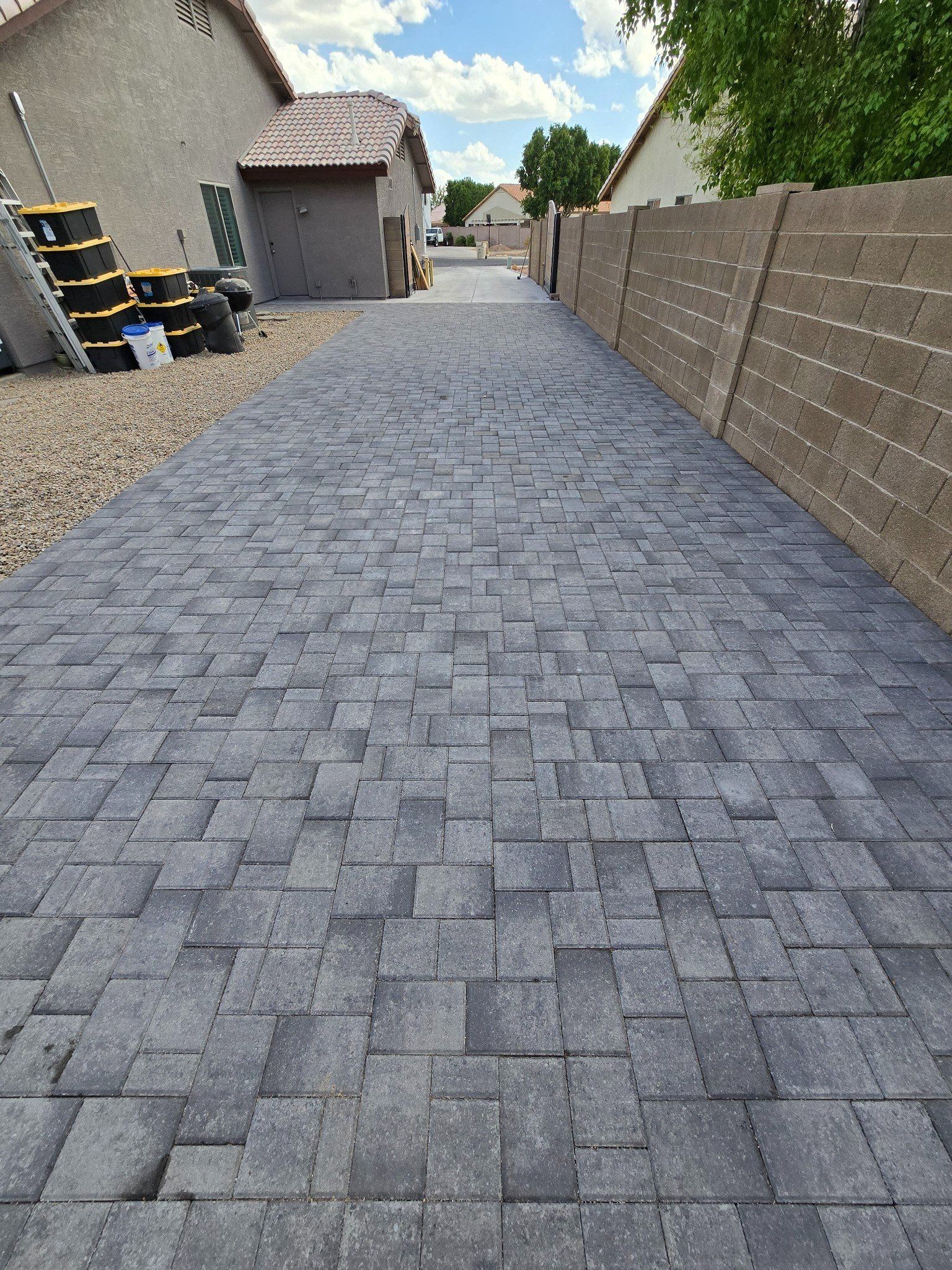 A brick driveway leading to a house with a fence in the background.