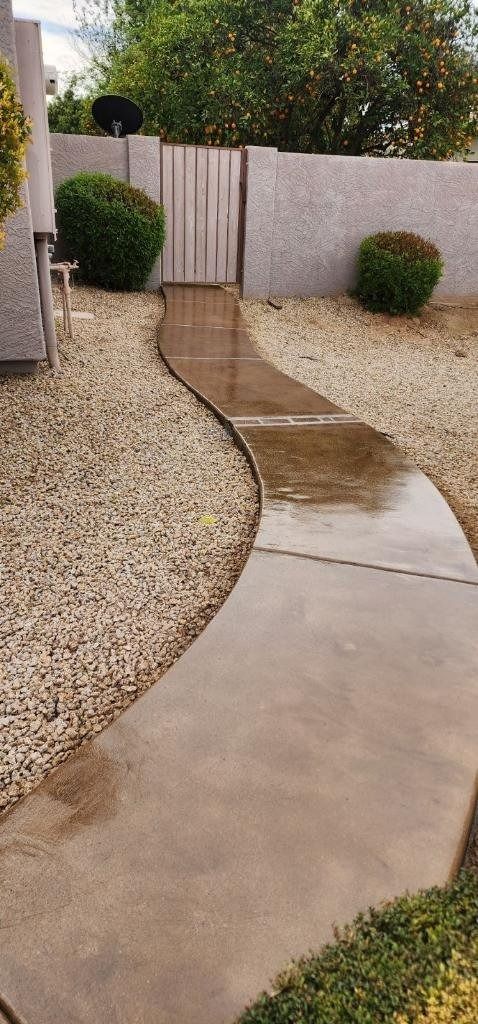 A concrete walkway leading to a gate in a backyard.