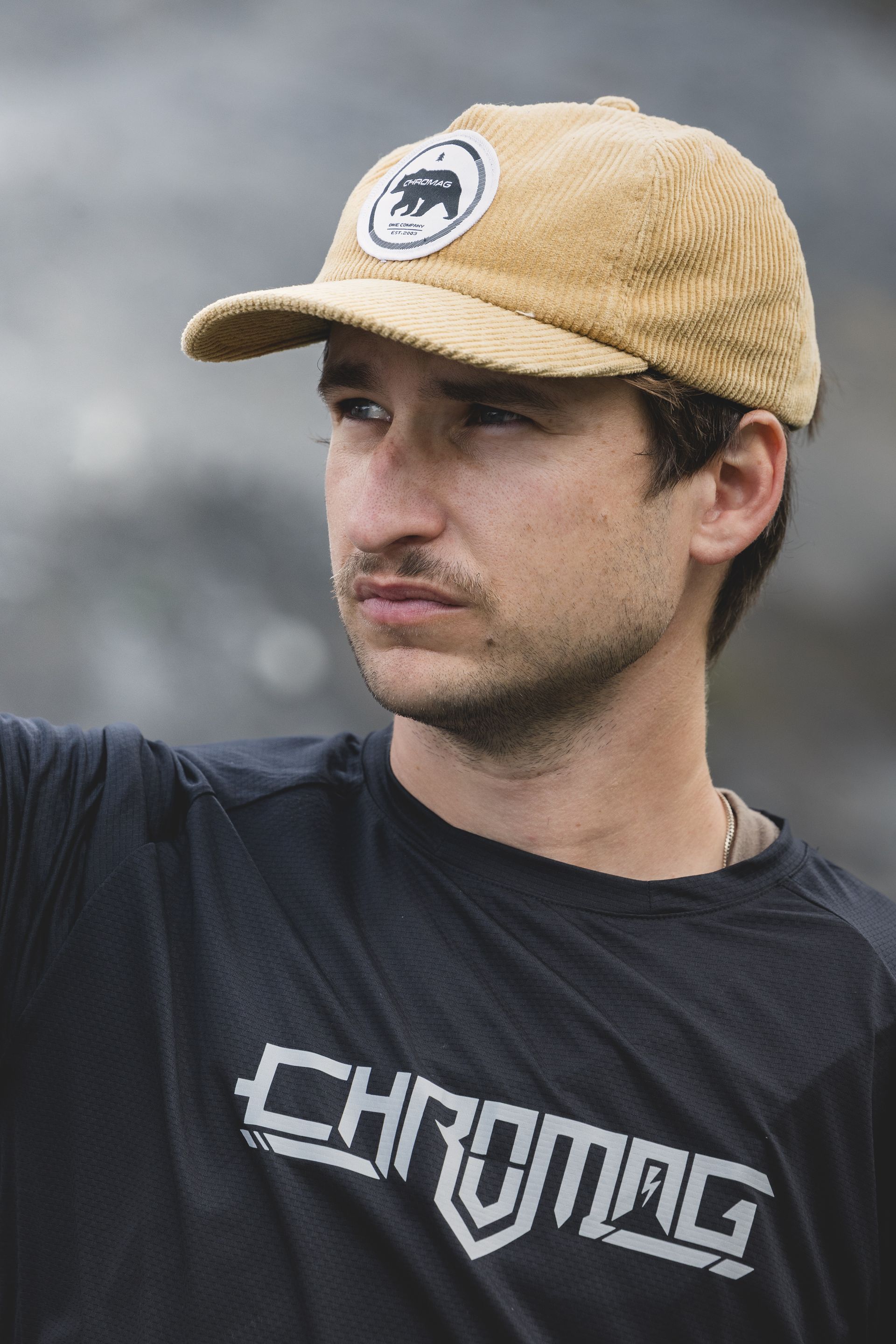 Man wearing tan cap and black Chromag t-shirt looks off to the side.