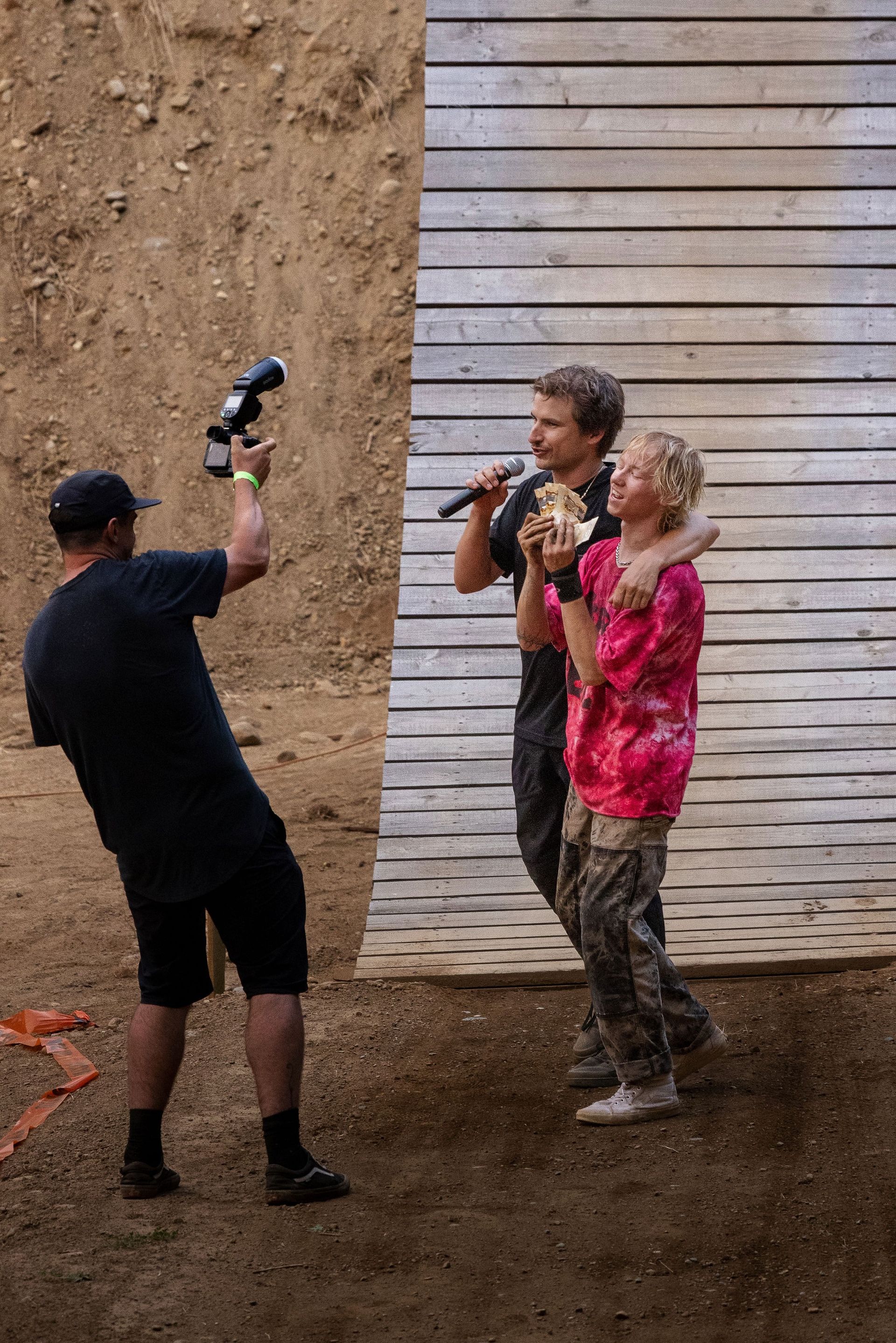 Photographer taking picture of two people on a stage; one with a microphone, the other hugging them.