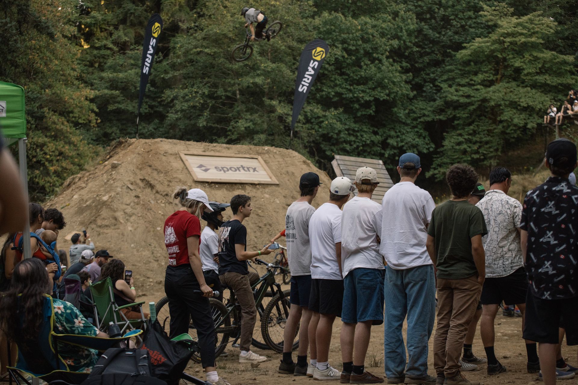 People watching a mountain bike competition. Rider in air above a dirt jump.