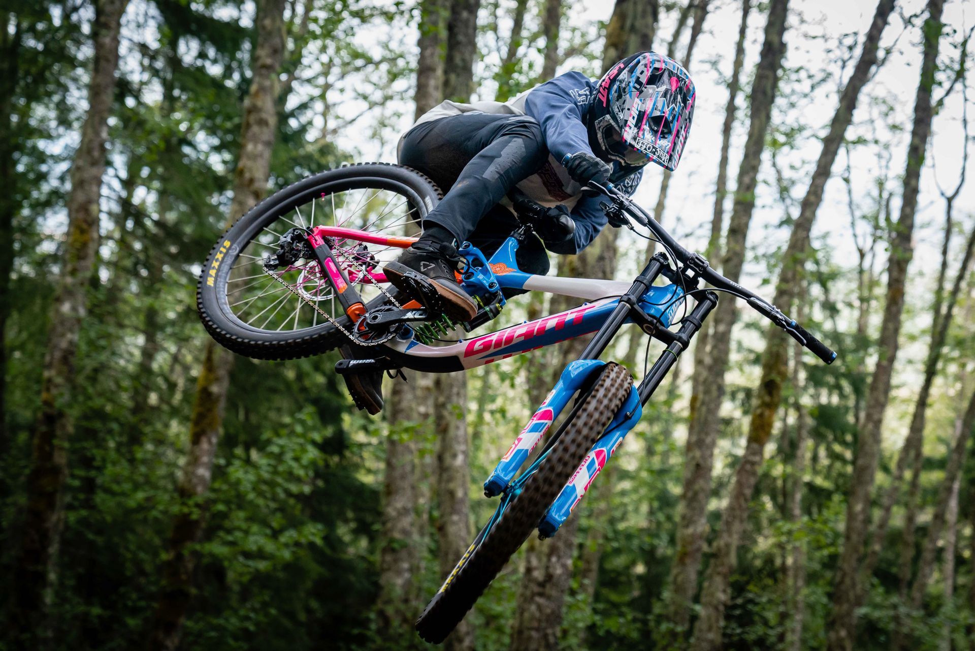 Mountain biker airborne in a forest, performing a jump, wearing a helmet and colorful bike.