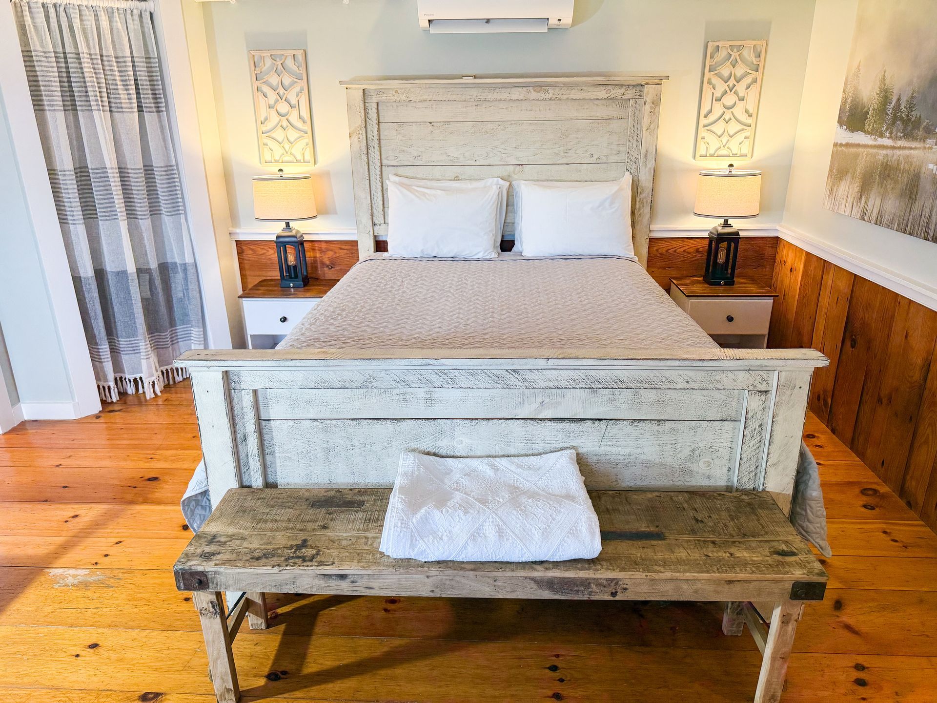Bedroom with a rustic, white-painted bed, wood floors, and two matching nightstands with lamps.
