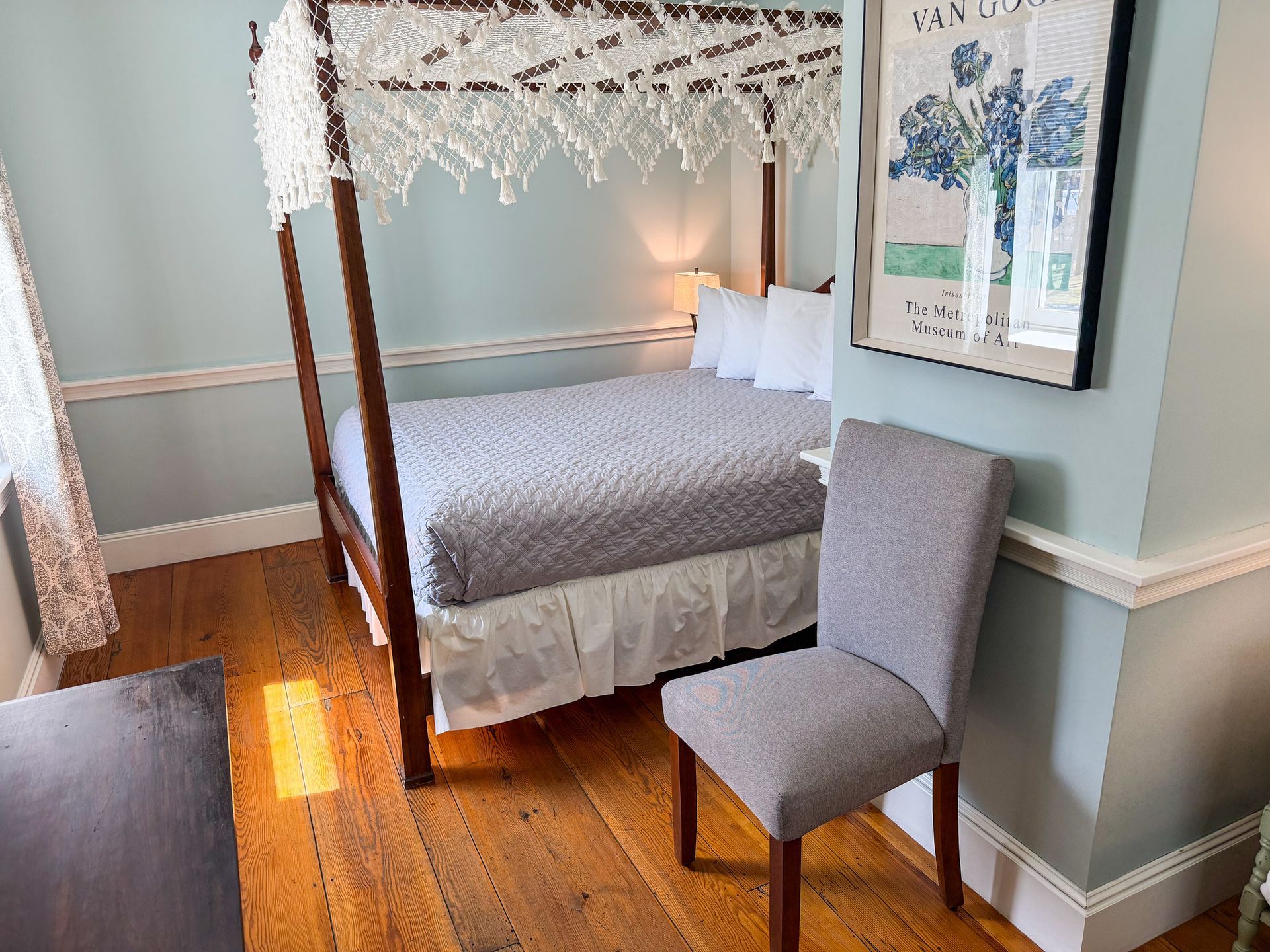A bedroom with a four poster bed and a chair.