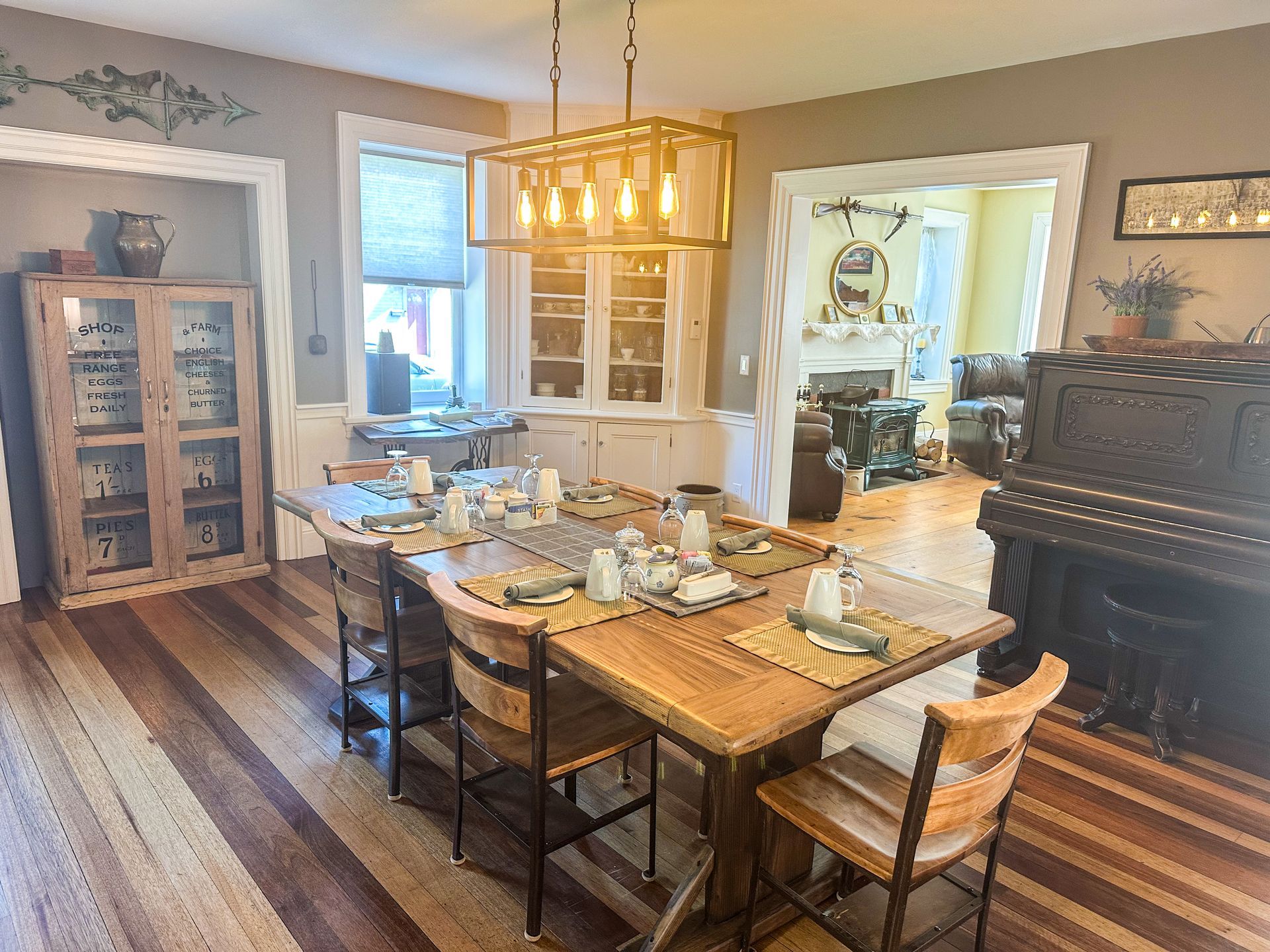 A dining room with a wooden table and chairs and a piano.