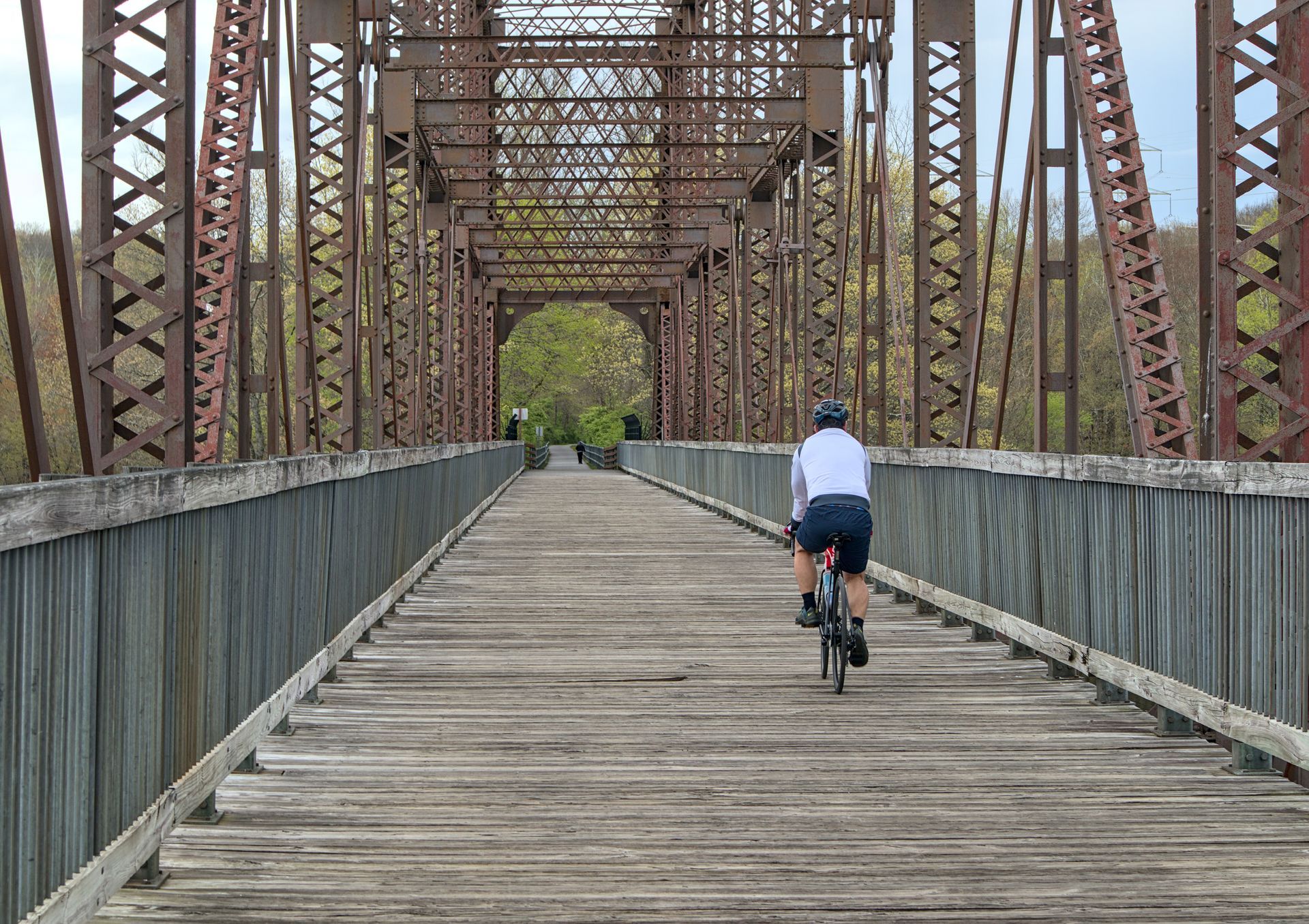 Cyclist rides across a wooden bridge with rusted metal supports.