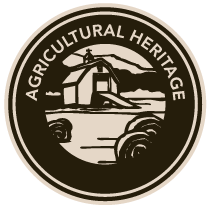 An agricultural heritage logo with a barn and hay bales in a circle.