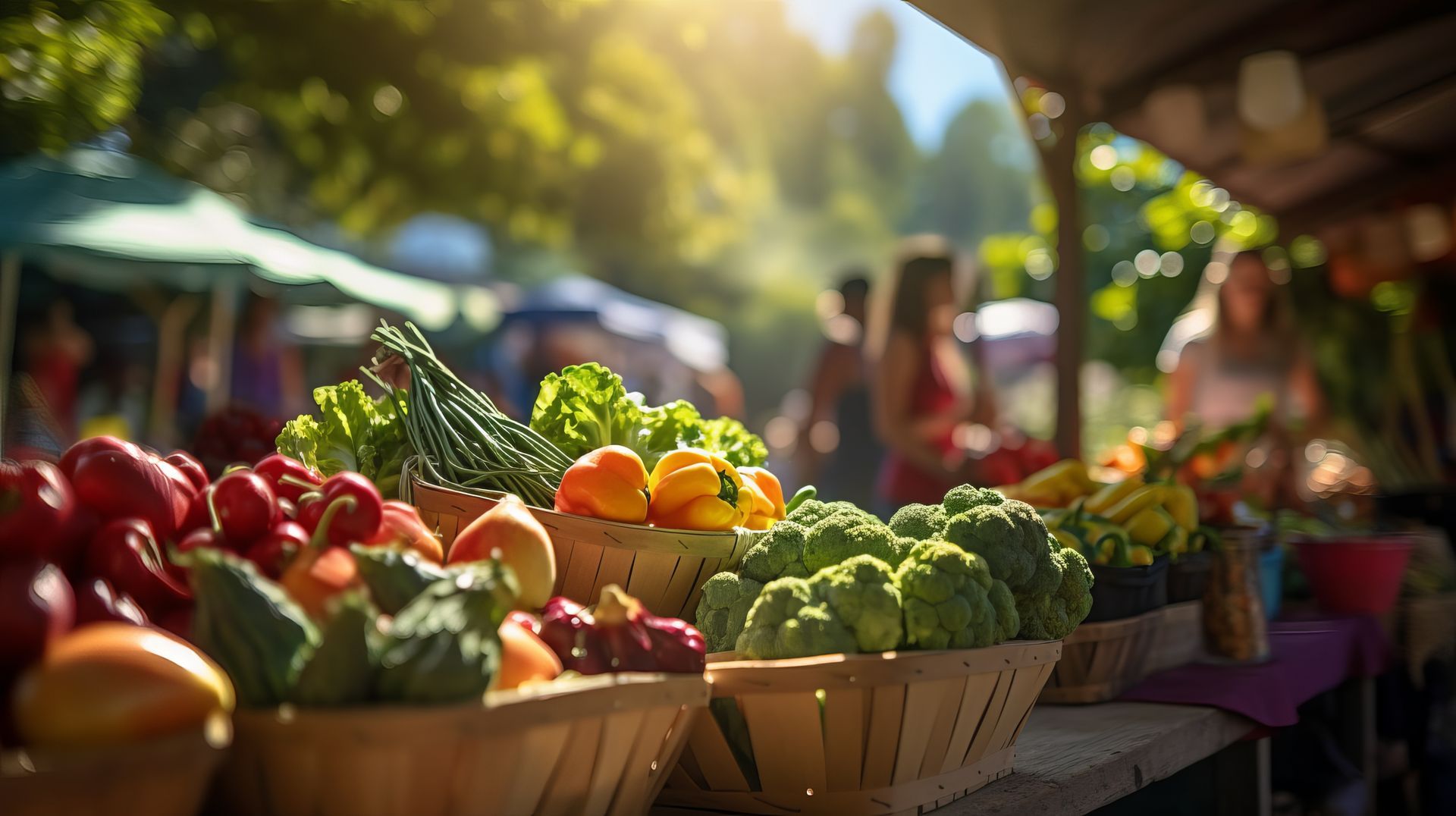 Produce displayed in baskets at a farmer's market, with customers browsing in the background on a sunny day.