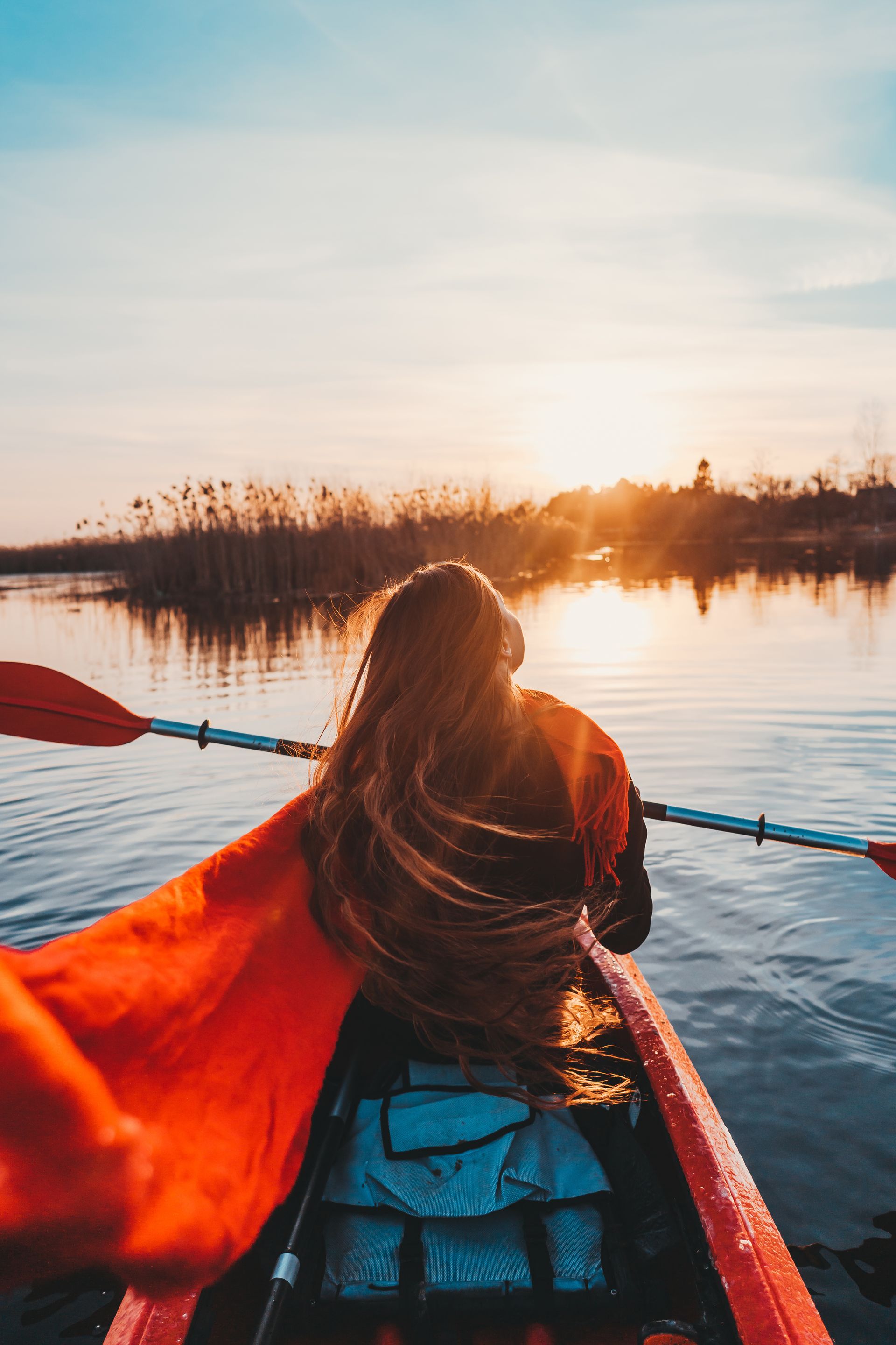 Person paddling a red canoe on a calm lake at sunset