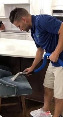 A man is cleaning a chair with a vacuum cleaner in a kitchen - Macomb, MI - Night Owl Express Carpet Cleaning