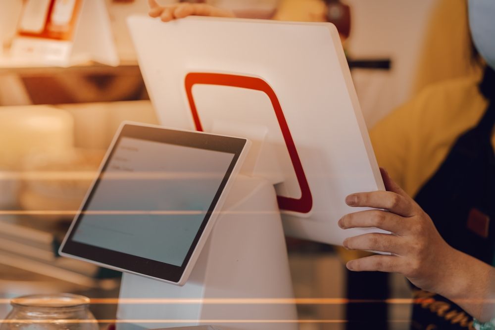 A person is holding a tablet in front of a computer monitor.