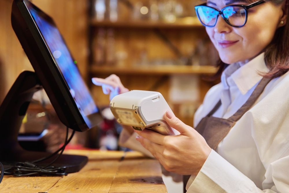 A woman is using a credit card reader in front of a computer.