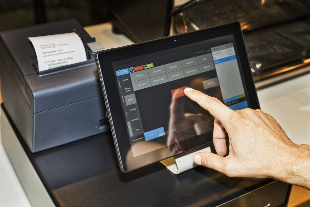 A person is using a tablet with a printer in the background.