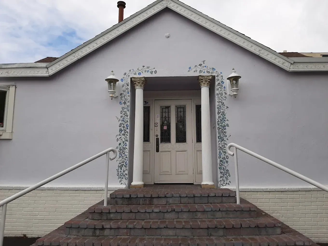 Front entrance of a white house with steps, railings, and a centered door under a peaked roof