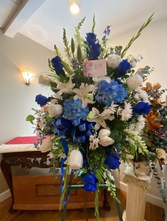 Blue and white funeral flower arrangement on a stand in an indoor room