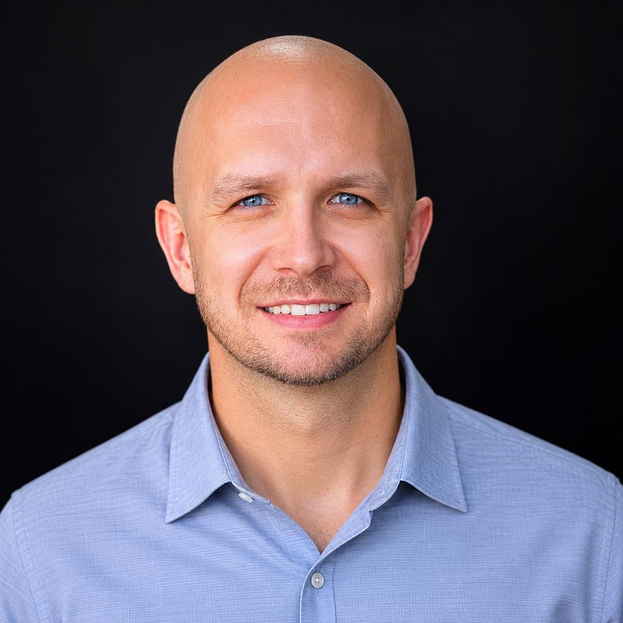 Smiling bald man in a light blue shirt on a dark background