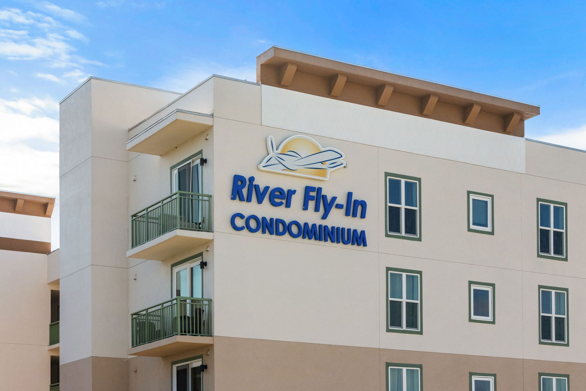 River Fly-in Condominiums building exterior with blue logo and balconies under a clear sky