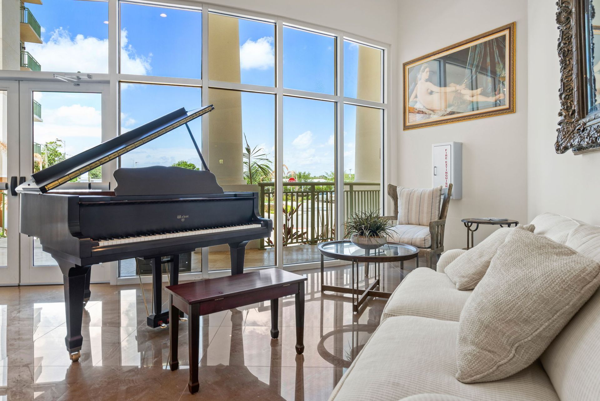 Bright living room with a grand piano, white sofa, and large windows overlooking a balcony.