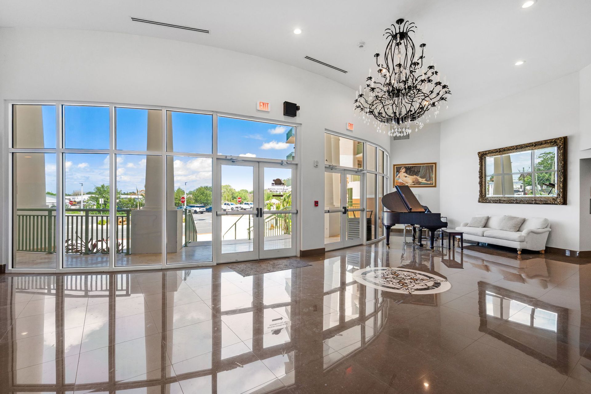 Bright living room with glossy floors, piano, chandelier, white sofa, and large glass doors to a balcony.