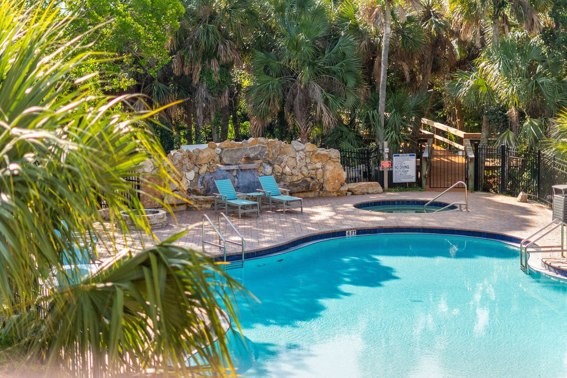 Outdoor swimming pool with blue water, two lounge chairs, and tropical landscaping