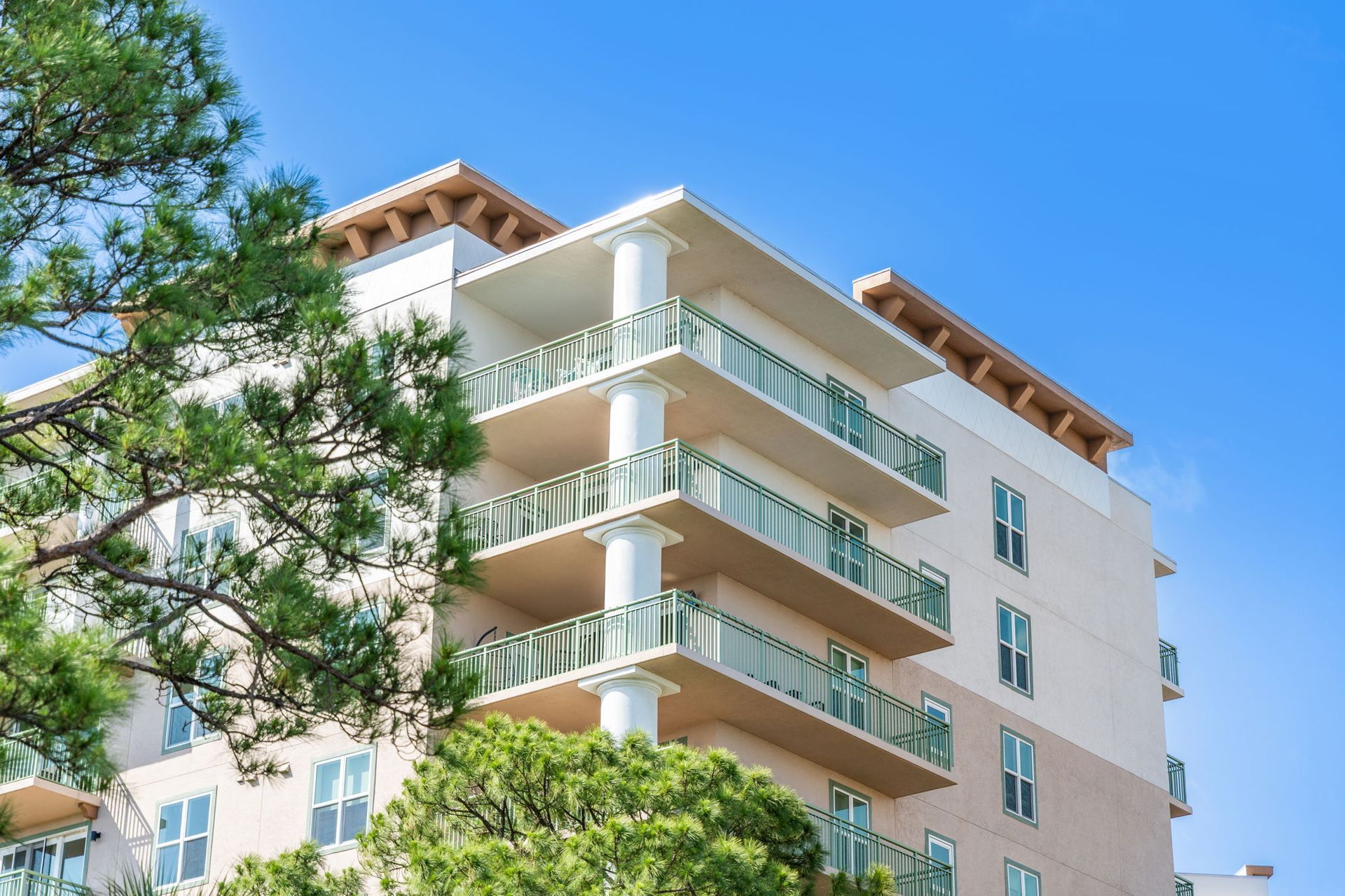 Modern beige condominium building in Merritt Island with balconies and green trees against a blue sky