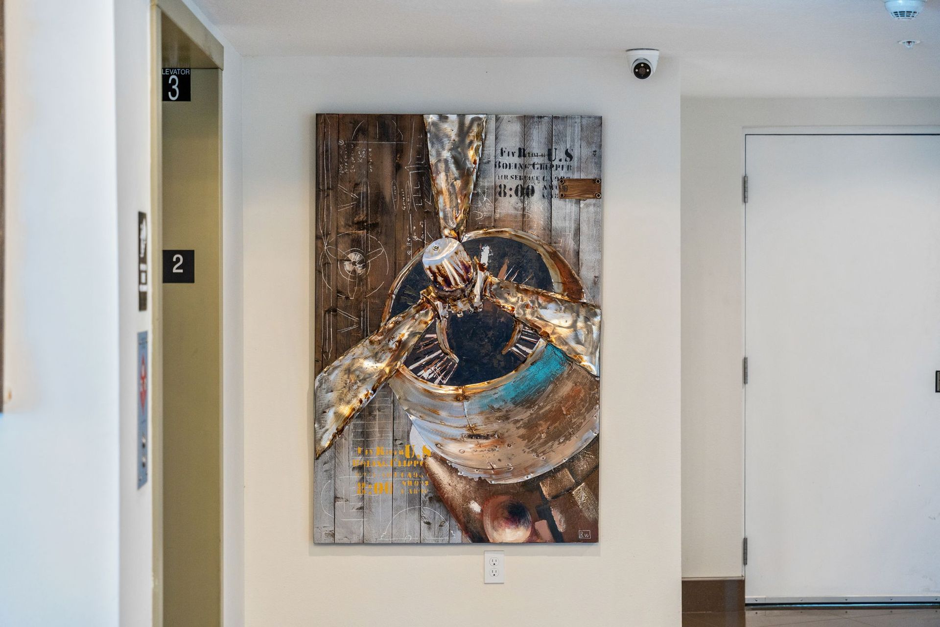 Abstract wall art in a white hallway with an elevator on the left and a closed door on the right