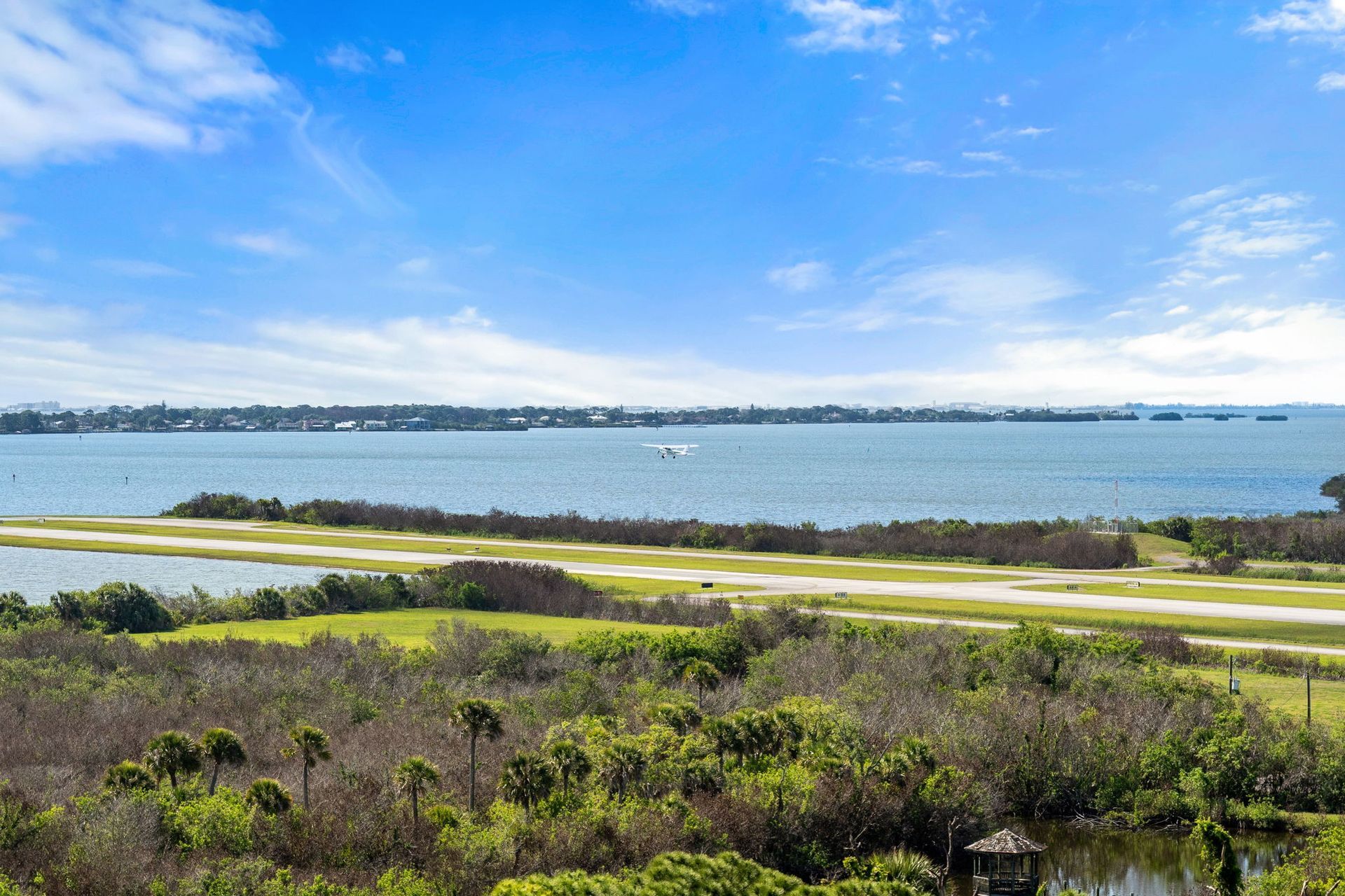 Coastal landscape with blue sky, calm bay, sandy path, and green vegetation in the foreground