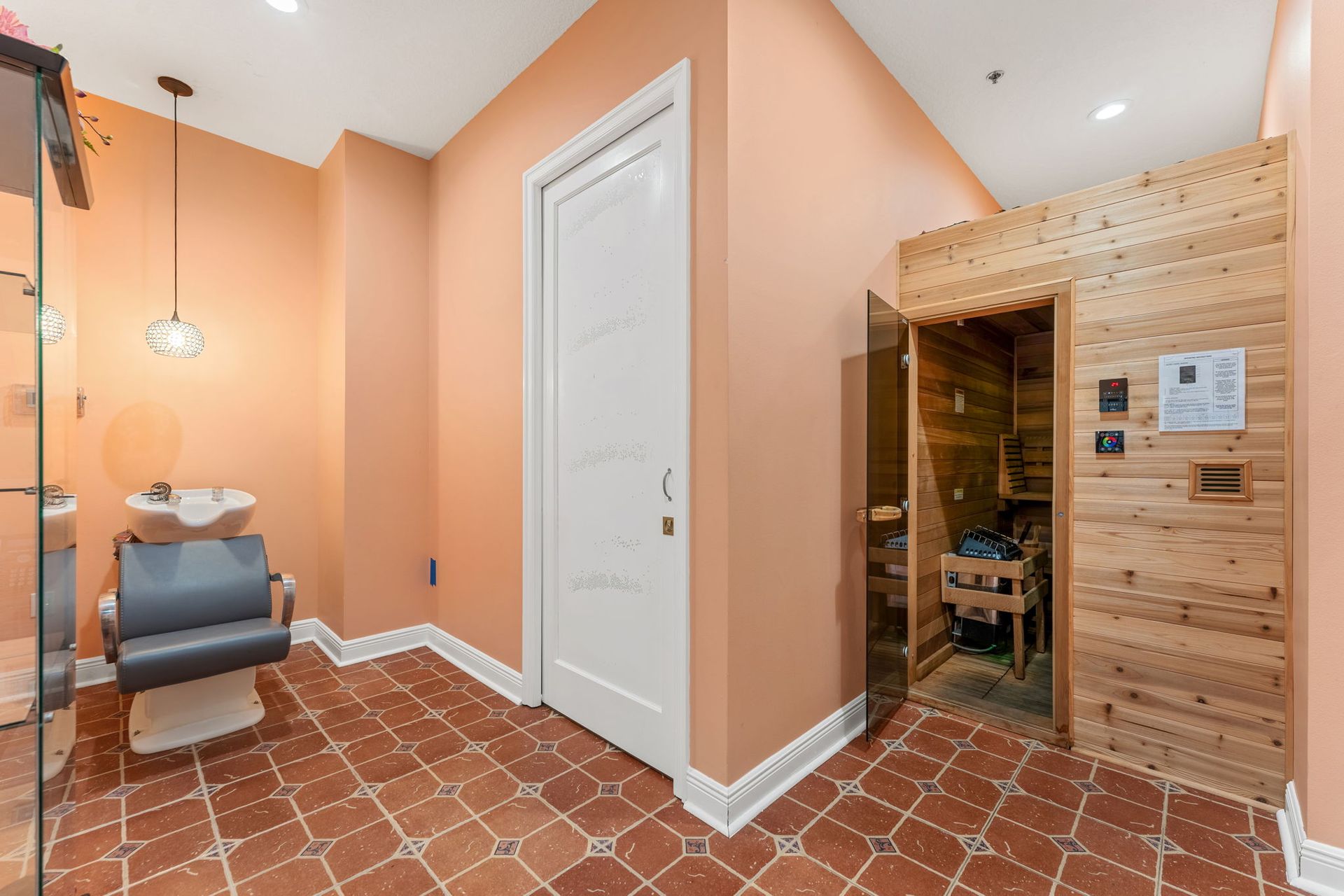 Peach spa room with massage chair, white door, and wooden sauna entrance on terracotta tile floor