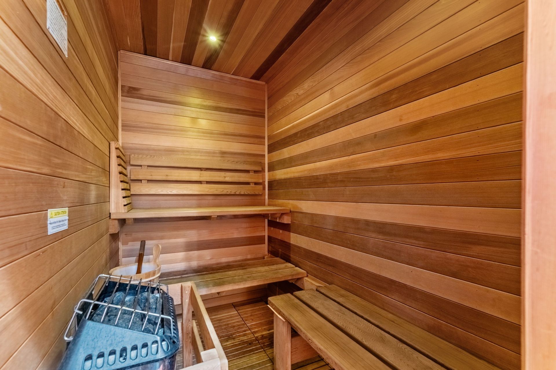 Wood-paneled sauna interior with wooden benches and a metal heater basket in the corner