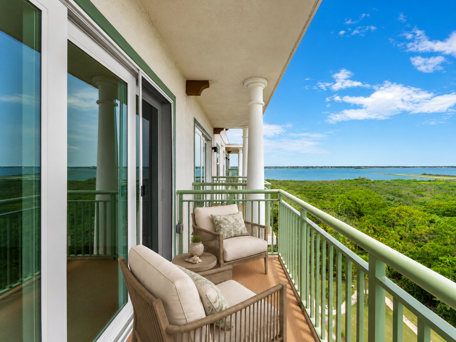 Balcony with wicker chairs overlooking lush green treetops and a blue ocean under a clear sky