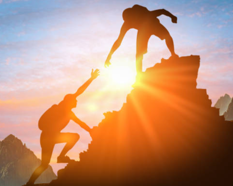 a man is helping another man climb a mountain .