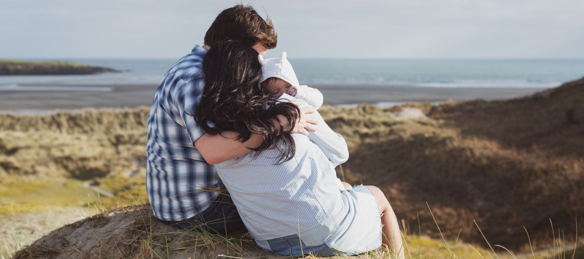 A man and a woman are sitting on top of a hill hugging each other.