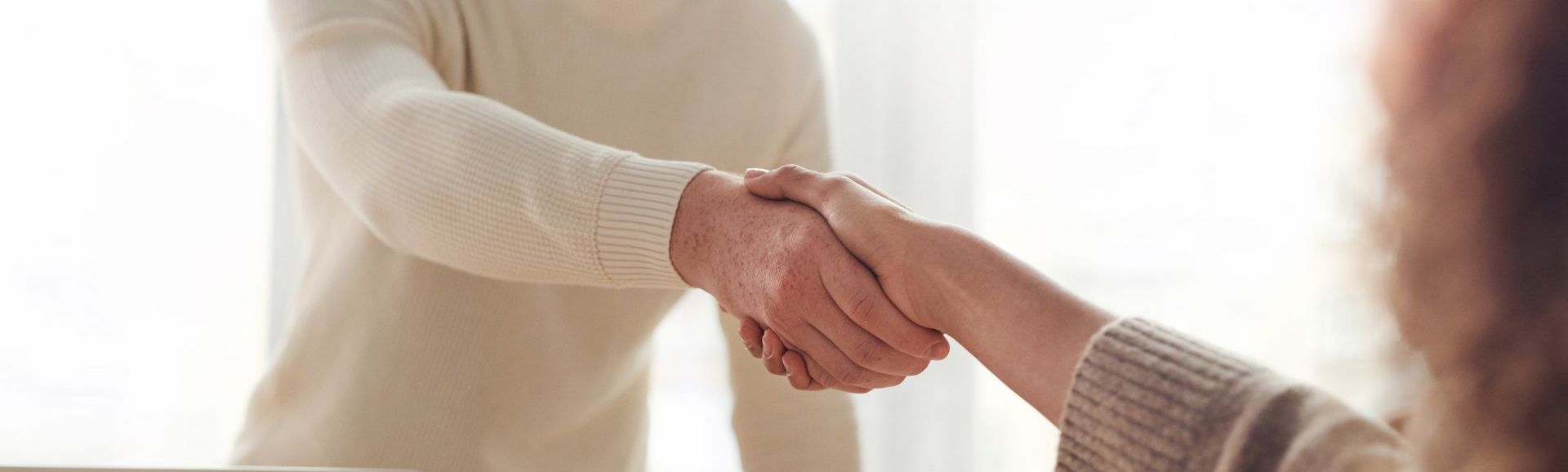 A man and a woman are shaking hands in front of a window.